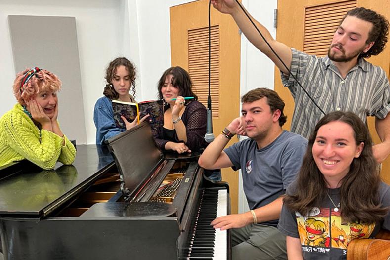 Student's from Joel Brown's class gather around a piano, posing.