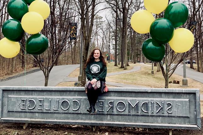 Melanie Nolan poses with the Skidmore sign at the entrance to the college campus